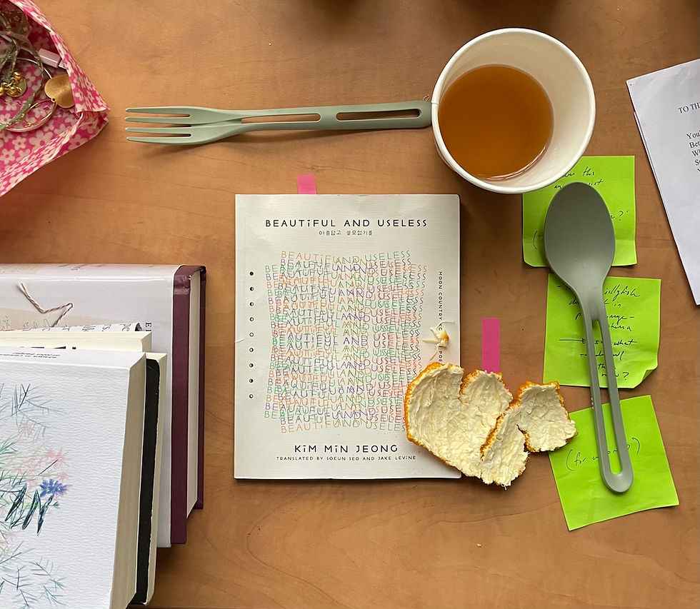 Beautiful and Useless sits on a wooden surface alongside cutlery, acid green sticky notes, orange peel, a half-drunk cup of tea and other books.