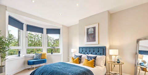 Large bright master bedroom with bay window, decorated in rich navy and gold.