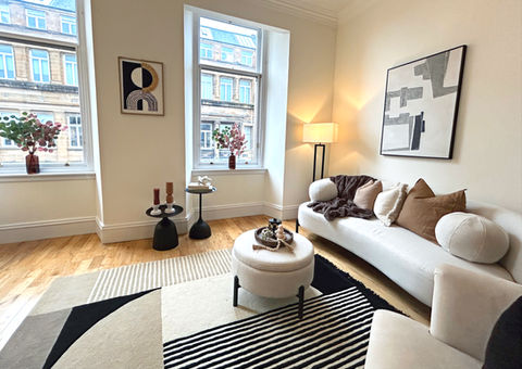 Professionally staged living room with cream sofa, modern decor, and large windows.