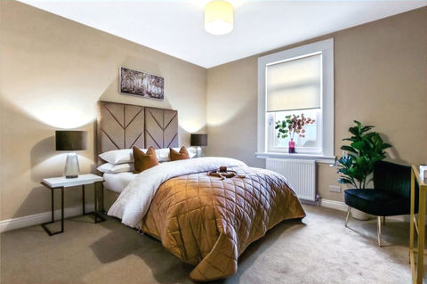 Staged master bedroom with neutral tones and warm accents in a professionally styled Glasgow show home.