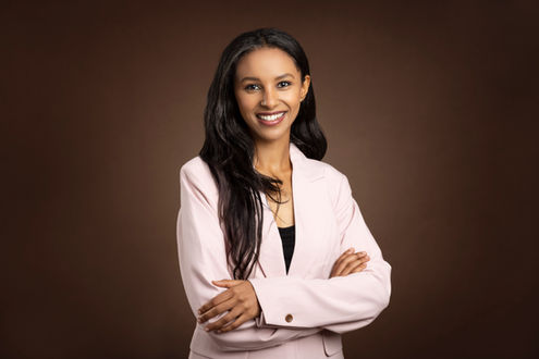 Professionelt portræt af kvinde i lyserød blazer med armene over kors, brun baggrund.