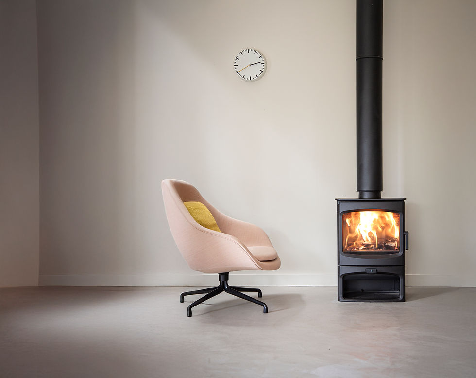 Salon minimaliste : fauteuil rose, poêle à bois allumé, horloge murale, ambiance chaleureuse.
