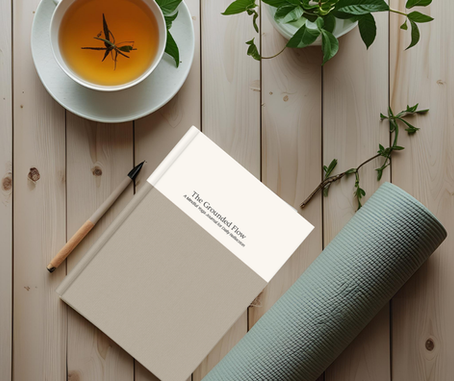 Tea, book titled "The Grounded Flow," a pen, green plant, and yoga mat on a wooden surface. Calm and serene setting.