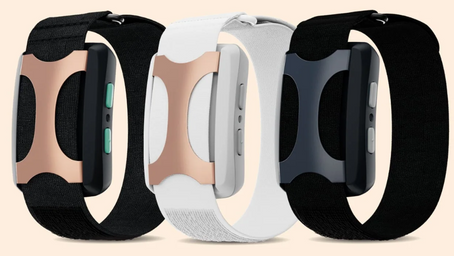 Three smart wristbands with black, white, and gold accents stand side by side on a beige background, showcasing their sleek design.