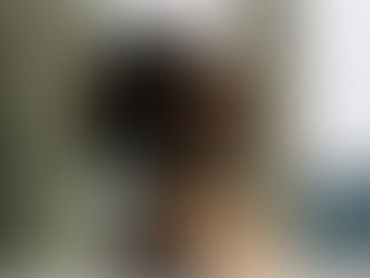 A person with closed eyes peacefully enjoys sunlight by a window, wearing a brown shirt. Soft lighting, serene mood.