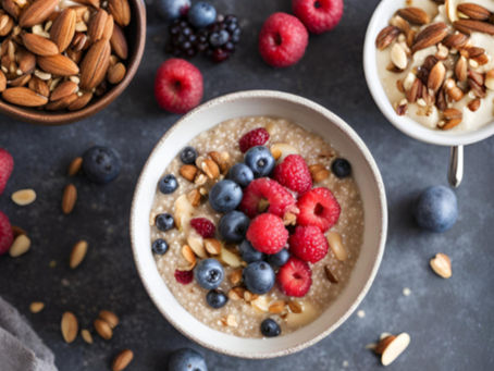 Bowl of oatmeal topped with raspberries, blueberries, almonds on a dark background. Another bowl with almonds and yogurt nearby. Vibrant colors.