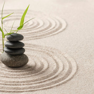 Stacked stones with green leaves in raked sand, forming circular patterns. The serene setting conveys a sense of balance and calmness.