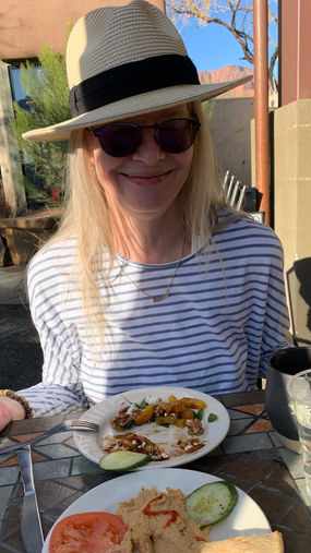Woman wearing hat and sunglasses smiles while at a restaurant table