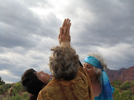 Three women staning in a circle reach their linked hands upward as the gaze into the sky.