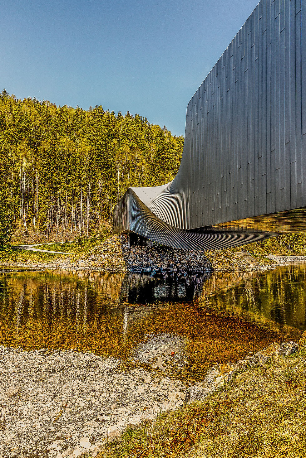 Moderne arkitektur over vannet med reflekser, Atelie Melheim, skog i bakgrunnen.