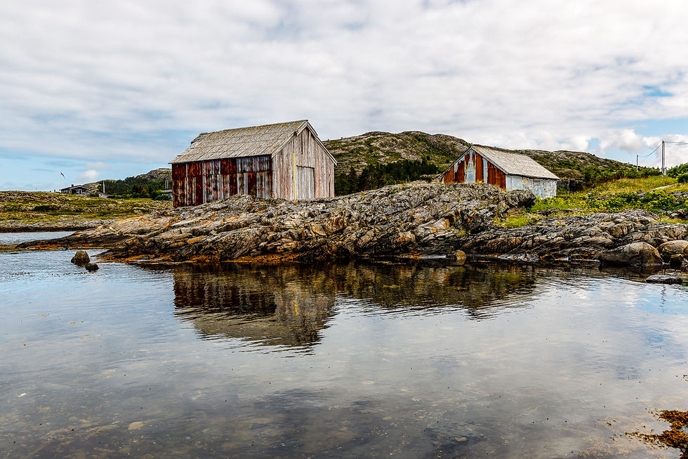 De værslitte røde naustene speiler seg i det rolige , lave vannet , mens de venter på neste flo.