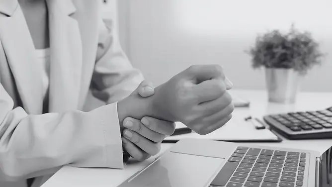 Woman in an office gripping her wrist due to carpal tunnel pain while working at a desk