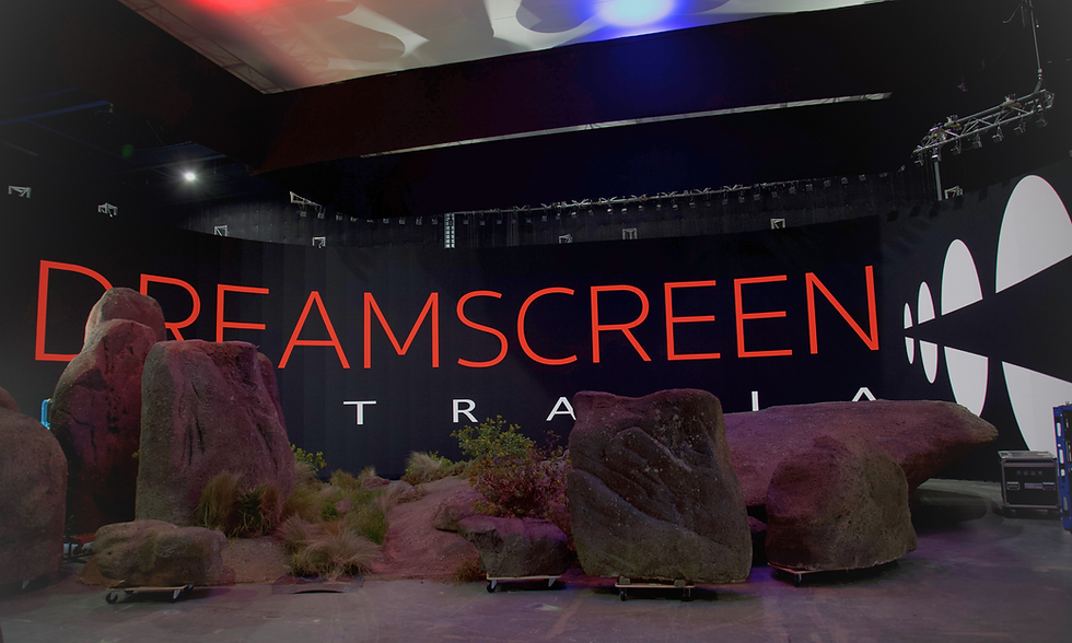 Stage with large rocks and bushes, set against a black backdrop with "DREAMSCREEN" in red letters. Overhead lights cast a colorful glow.