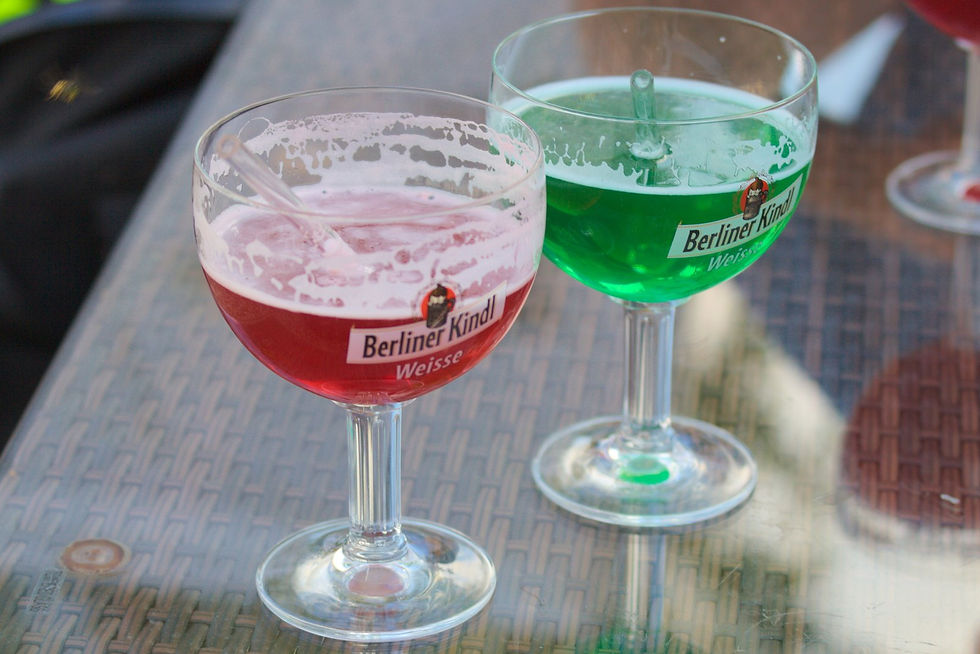 Two glasses of Berliner Weisse mit Schuss, one bright red with raspberry syrup and one green with woodruff syrup