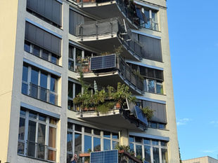 A Berlin apartment block on Lübecker Strasse in Moabit with solar panels on six balconies, some flat against the railing and some tilted out, in evening light