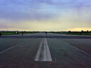 The old Tempelhof runway at dusk, its painted centre line running towards a low orange horizon