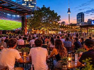 A summer evening football public viewing in Berlin with a relaxed crowd, outdoor screen and TV Tower skyline