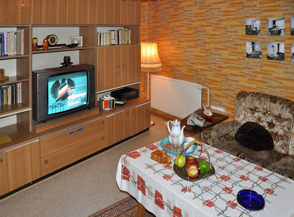 A reconstructed 1980s East German living room inside the DDR Museum, with a wood wall unit, boxy television, orange wallpaper and a floral sofa