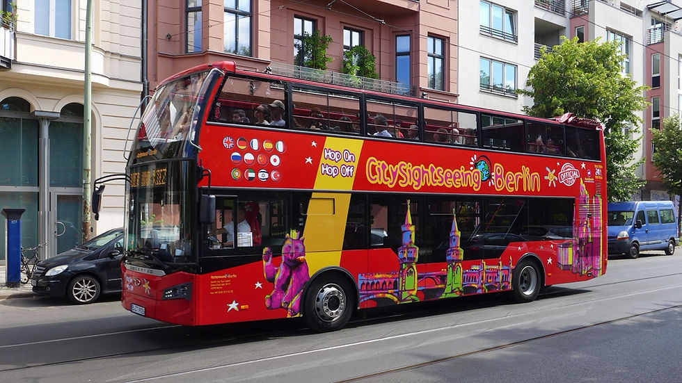 A red City Sightseeing Berlin open-top double-decker with passengers on the upper deck in summer