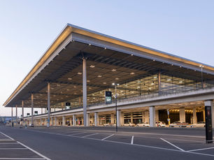 Berlin Brandenburg Airport Terminal 1 at dusk, with the long glass frontage and the curbside pickup lane where ride apps and taxis wait