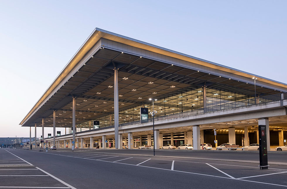 Berlin Brandenburg Airport Terminal 1 at dusk, with the long glass frontage and the curbside pickup lane where ride apps and taxis wait