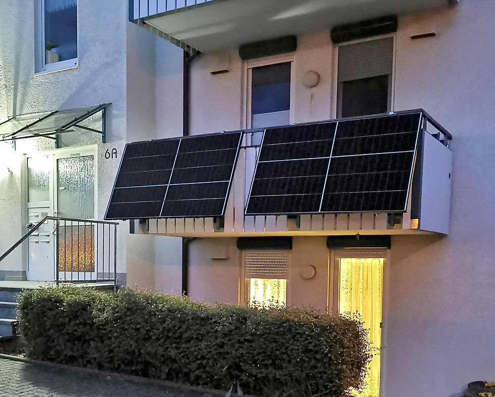 Two solar modules angled out from a balcony railing at dusk, with warm light coming from the window behind them