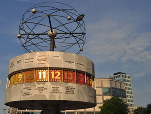 The Urania World Clock on Alexanderplatz in Berlin, its metal cylinder marked with world cities above a lit band of hour numbers running past 12, 13, 14 and 15.