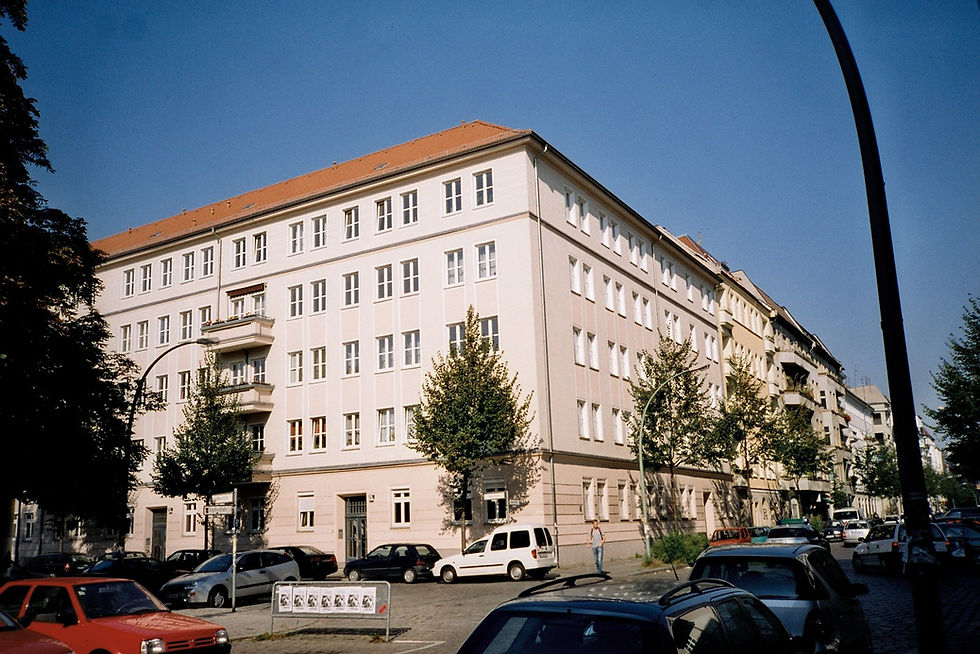 A pale post-war apartment block at Wismarplatz in Friedrichshain, built in the 1950s, with cars parked along the kerb