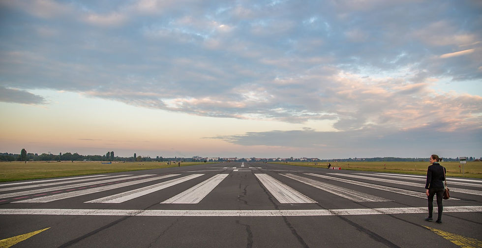 A single person walking down a disused runway at Tempelhofer Feld under a wide evening sky