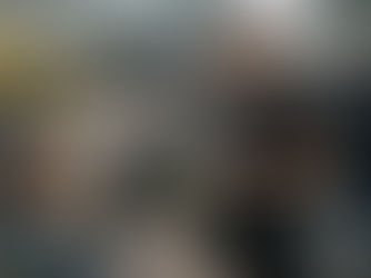 A waiter takes an order from a seated woman at an outdoor café. A yellow tram passes in the background. The scene is bustling and urban.