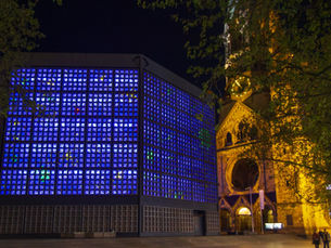 The blue-lit modern church and the floodlit broken old tower of the Kaiser Wilhelm Memorial Church at night on Breitscheidplatz