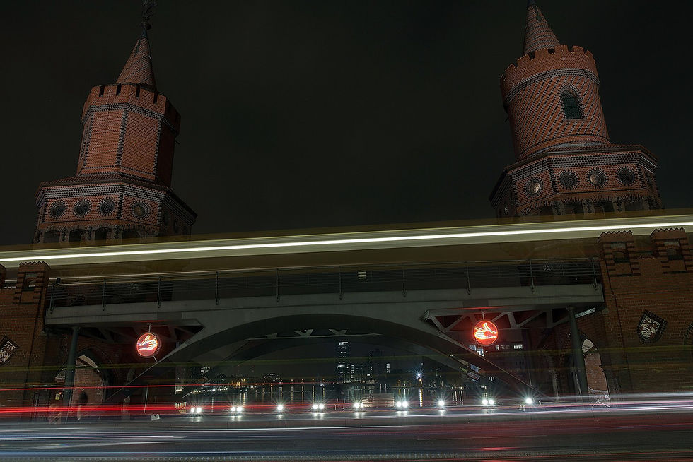 The Oberbaumbrücke at night, its brick towers lit and traffic light trails crossing beneath the U-Bahn viaduct
