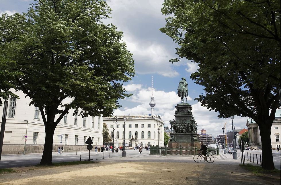 Unter den Linden boulevard in Berlin with trees, the Frederick the Great statue and the TV Tower in the distance