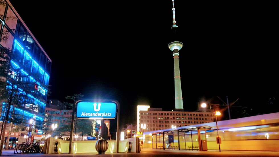 A tram passing the Alexanderplatz U-Bahn sign beneath the TV Tower at night