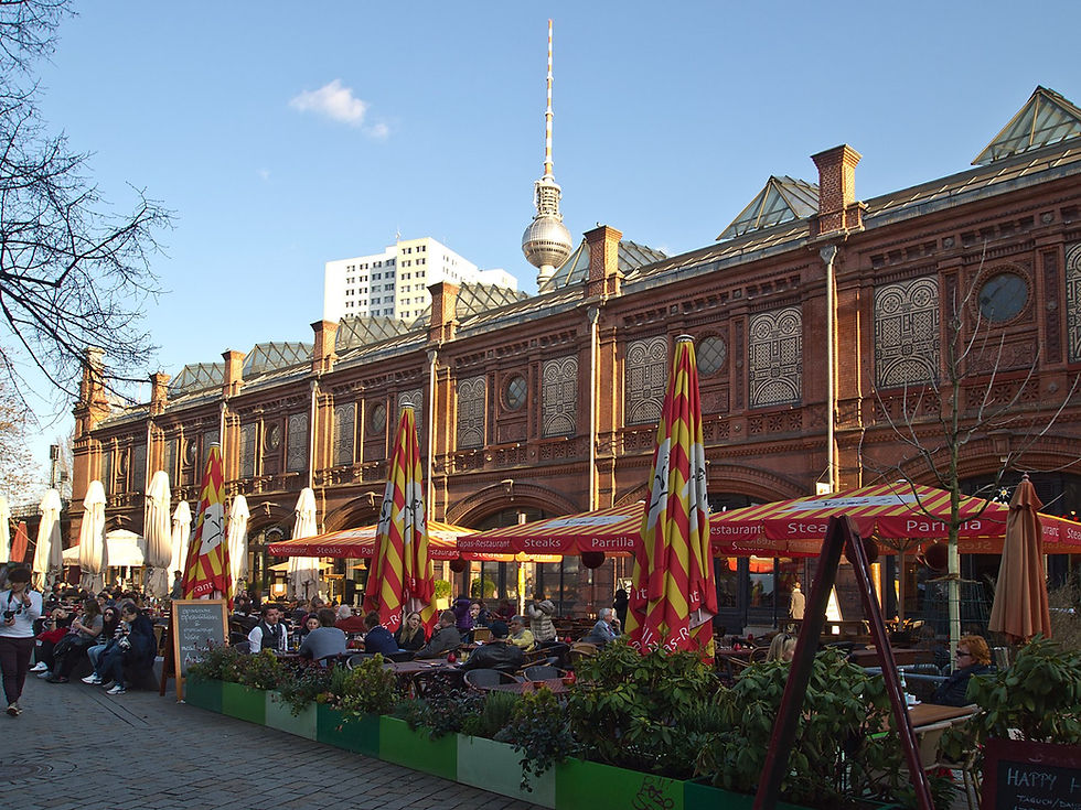 A busy terrace with colourful umbrellas at Hackescher Markt in Berlin, with the TV Tower behind the railway arches