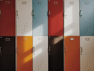 Colorful lockers in a grid pattern, featuring shades of red, blue, white, black, and orange. Sunlight casts shadows on the doors.