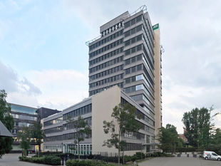 The AOK administration tower on Wilhelmstrasse in Berlin-Kreuzberg, a 1960s high-rise by Hans Scharoun and Bodo Fleischer, with the green AOK logo near the roof and a lower wing in front of it