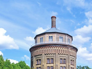 The Wasserturm, Berlin's oldest water tower, a round brick building on a green hill in Prenzlauer Berg under a summer sky