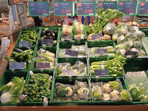 Fresh produce display inside a Berlin supermarket with prices and green vegetable crates