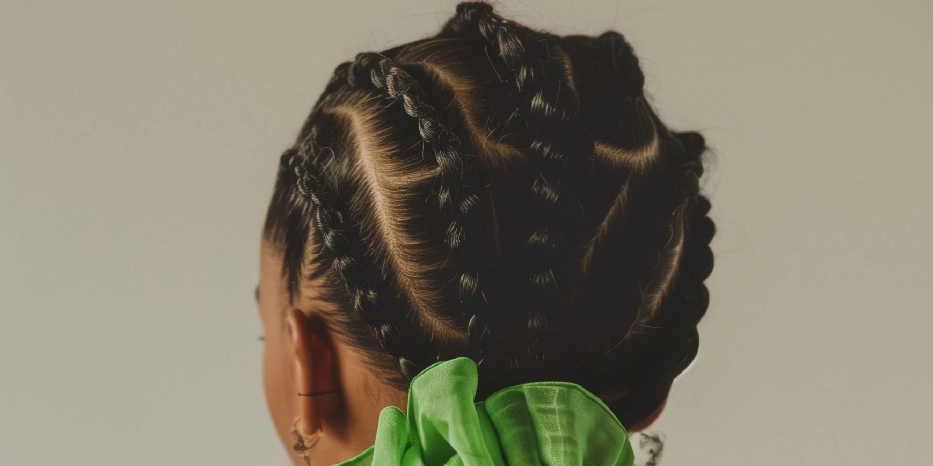 Aufwendig geflochtene Zöpfe in symmetrischem Muster, stilvoll fixiert mit einem grünen Haarband. Die Frisur kombiniert Präzision und Kreativität für einen modernen, eleganten Look.