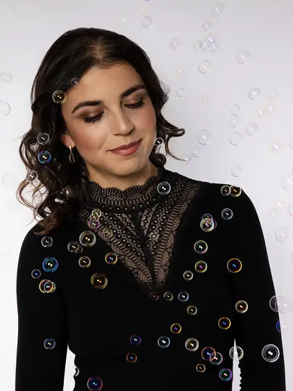 Studio Portrait mit Make Up, dunkles Oberteil, Spitzendetail, schwebende Seifenblasen, weiches Studiolicht, Fokus auf Material und Ausdruck.