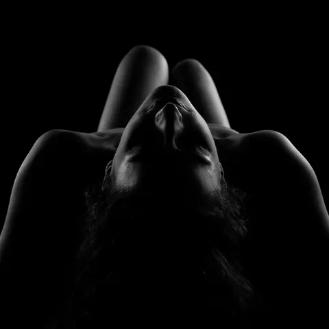 Schwarz-Weiß-Aufnahme einer Frau in Rückenlage, deren Gesicht durch Schatten hervorgehoben wird – minimalistisches Lichtspiel.