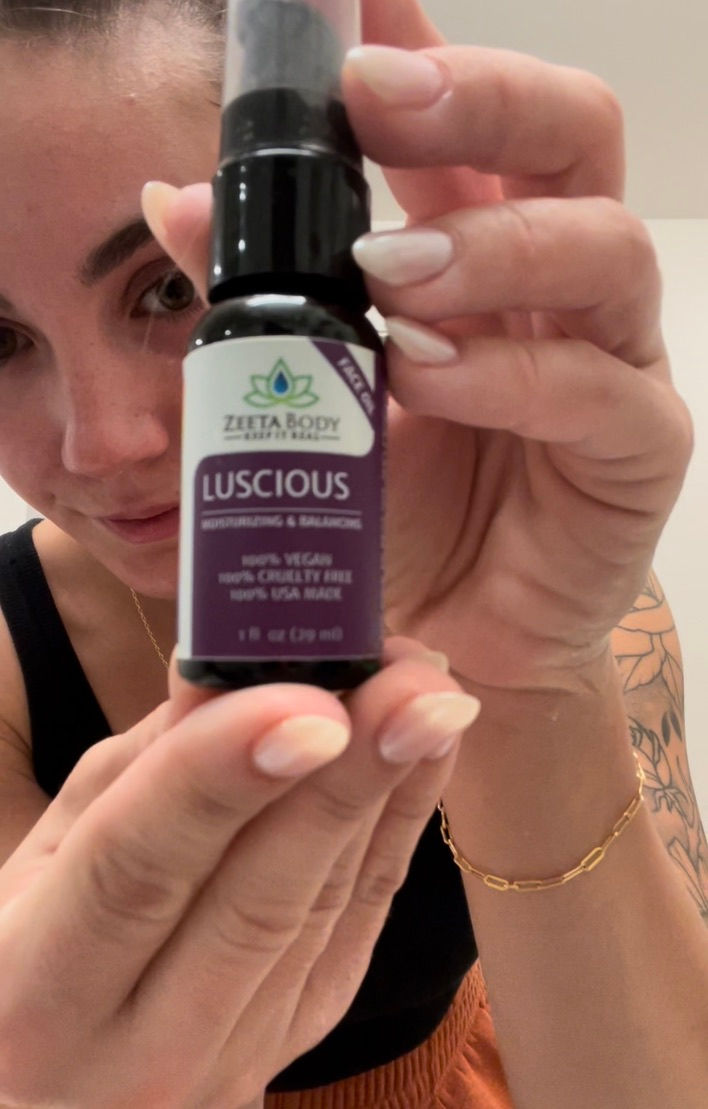 Woman holding a bottle of Zeeta Body Luscious face oil in a bathroom.