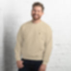 Lächelnder Mann im beigen Unisex Organic Creator Tee 2.0 vor weißer Ziegelwand