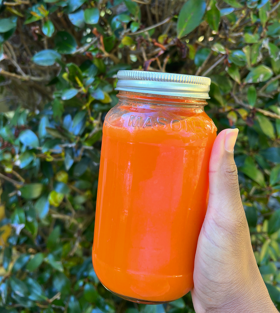 Hand holding an orange liquid-filled Mason jar against a green leafy background, creating a vibrant contrast.