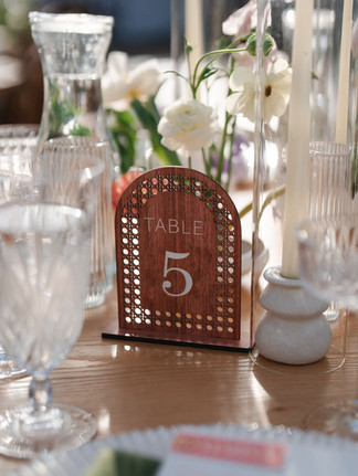 Detailed wedding coordinator table styling with modern wood table number, taper candles, and delicate white floral arrangements