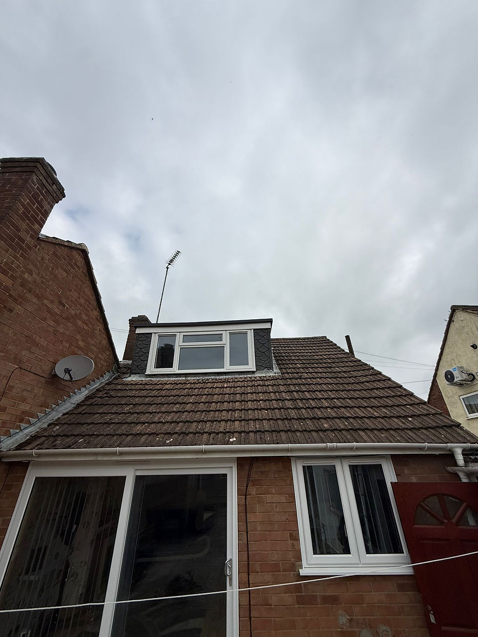 A garage with a brick wall and a silver metal roof, with a ladder and a pallet of materials on the driveway.