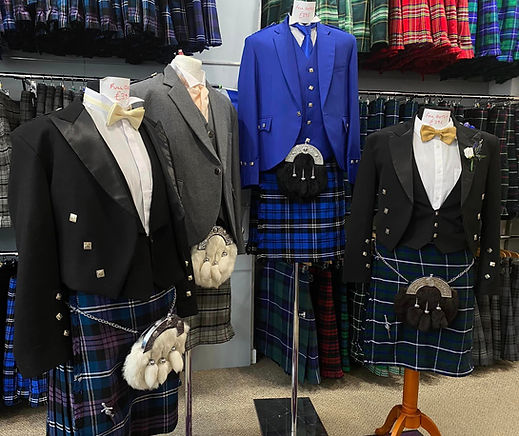 A selection of formal Highland dress jackets, including Prince Charlie and Argyll styles, displayed on mannequins in a clothing shop showroom