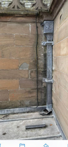 Close-up of a vertical metal pipe clamped against a stone wall