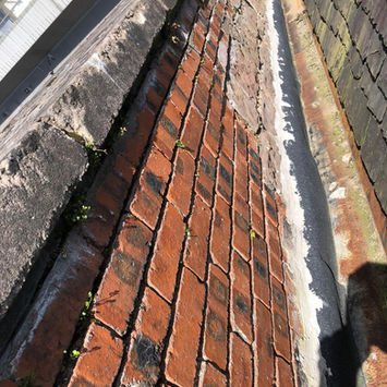 Narrow gully section between a red brick wall and roof slope